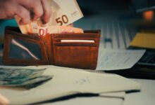 Hand placing euro banknotes into a brown leather wallet.