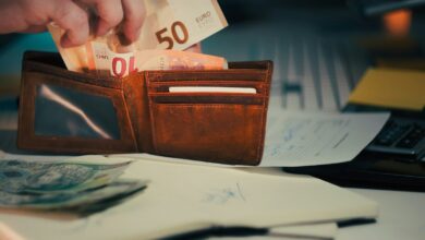 Hand placing euro banknotes into a brown leather wallet.