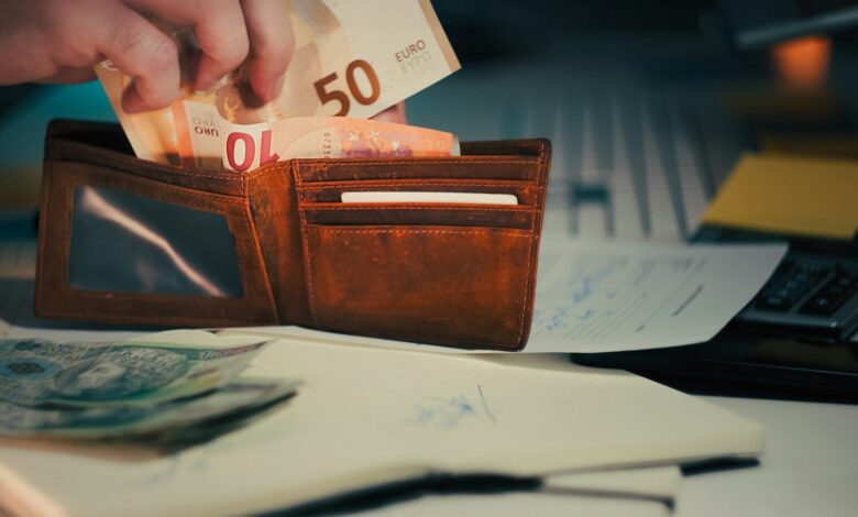 Hand placing euro banknotes into a brown leather wallet.